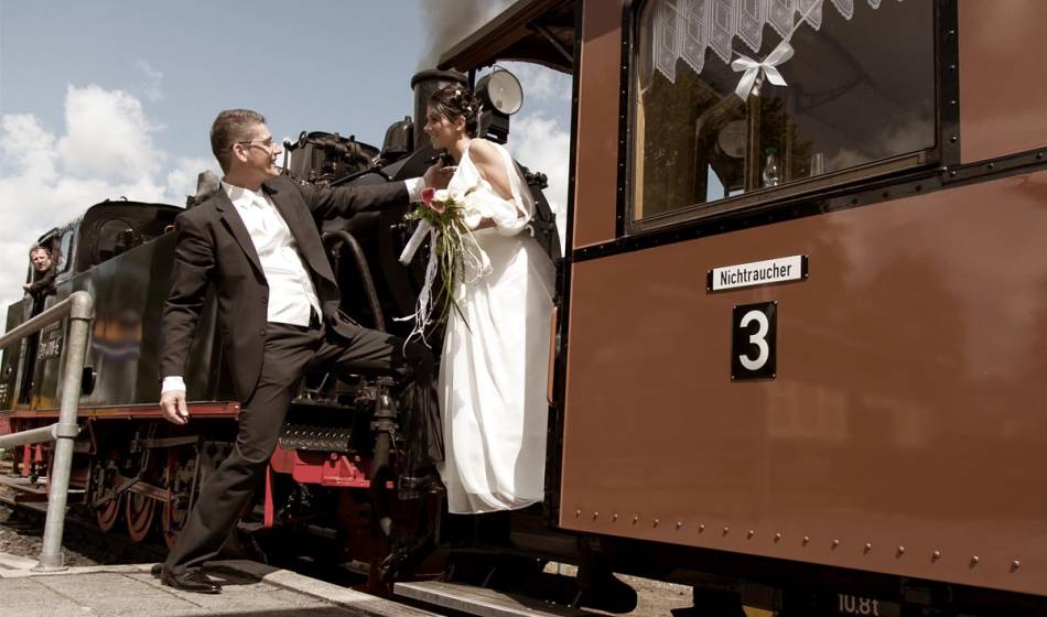 Wedding couple in festive clothing in front of a nostalgic steam train on Rügen, unique wedding motif.