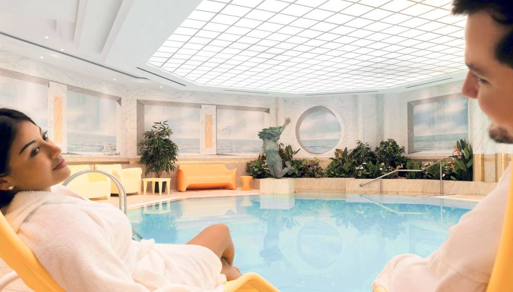 Wellnessbereich mit Thalasso-Feeling, ein Paar relaxt am Pool unter einem modernen Glasdach
