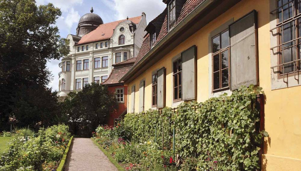 Goethes Wohnhaus mit Gartenweg, Blumenbeeten und Blick auf die Altstadt.