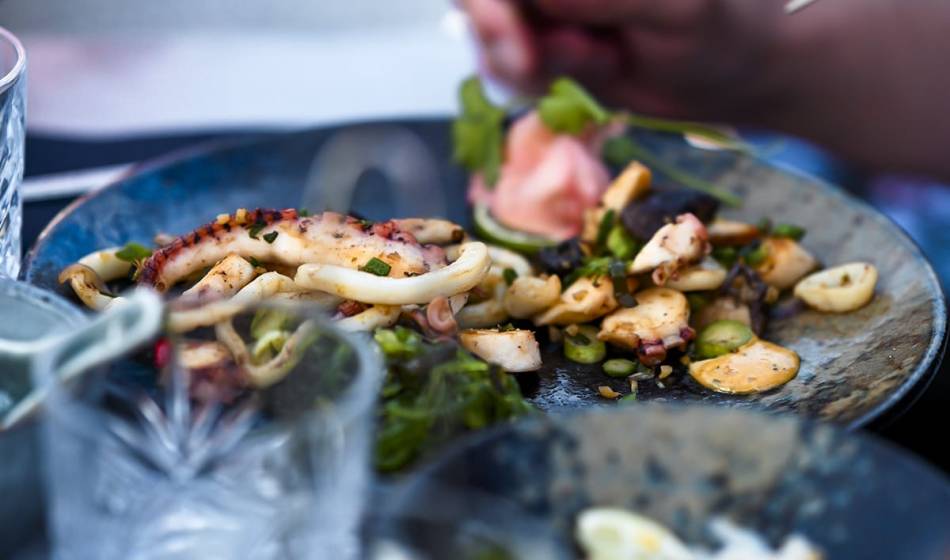 Plate of grilled seafood including squid and mussels decorated with herbs and vegetables at #herrhoshi restaurant.