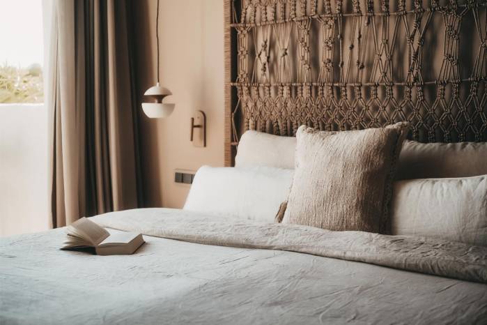 Cozy bed with decorative headboard, pillows and a book in the Lado Campo Suite at the Barefoot Hotel on Mallorca.