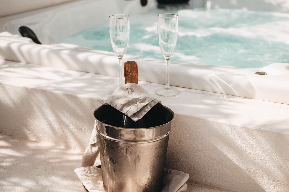 An ice bucket with a bottle of champagne and two glasses by the whirlpool, framed by sunlight in the Campo Lado Suite at the Barefoot Hotel.