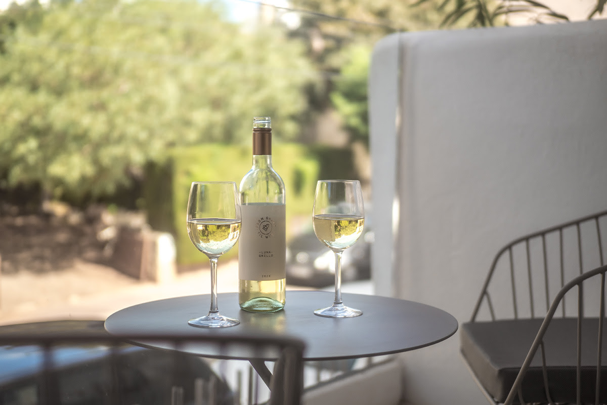 Bottle of white wine with two filled glasses on a table on the terrace of the double room Puerto at the Barefoot Hotel Mallorca.