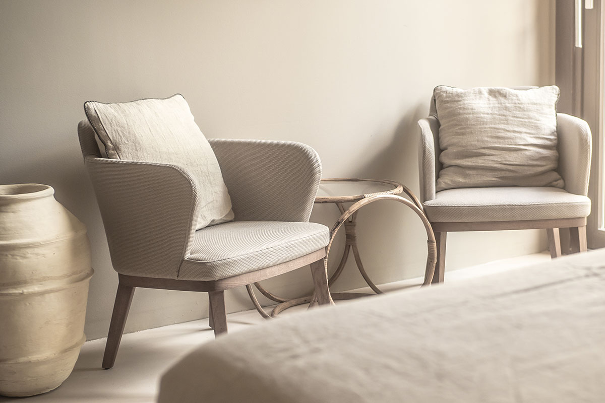 Two cozy armchairs with cushions, a natural wood table and warm lighting accents in the Puro room at the Barefoot Hotel Mallorca.