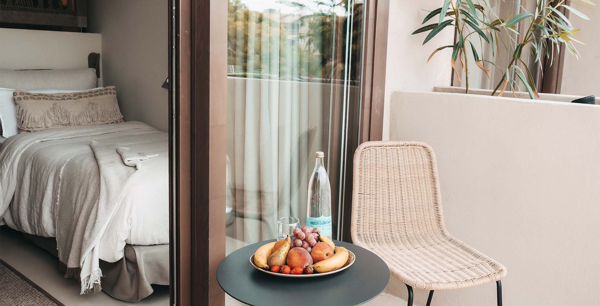 Dormitorio room in the Barefoot Hotel Mallorca with bed, balcony, a wicker chair and fruit bowl on the table.