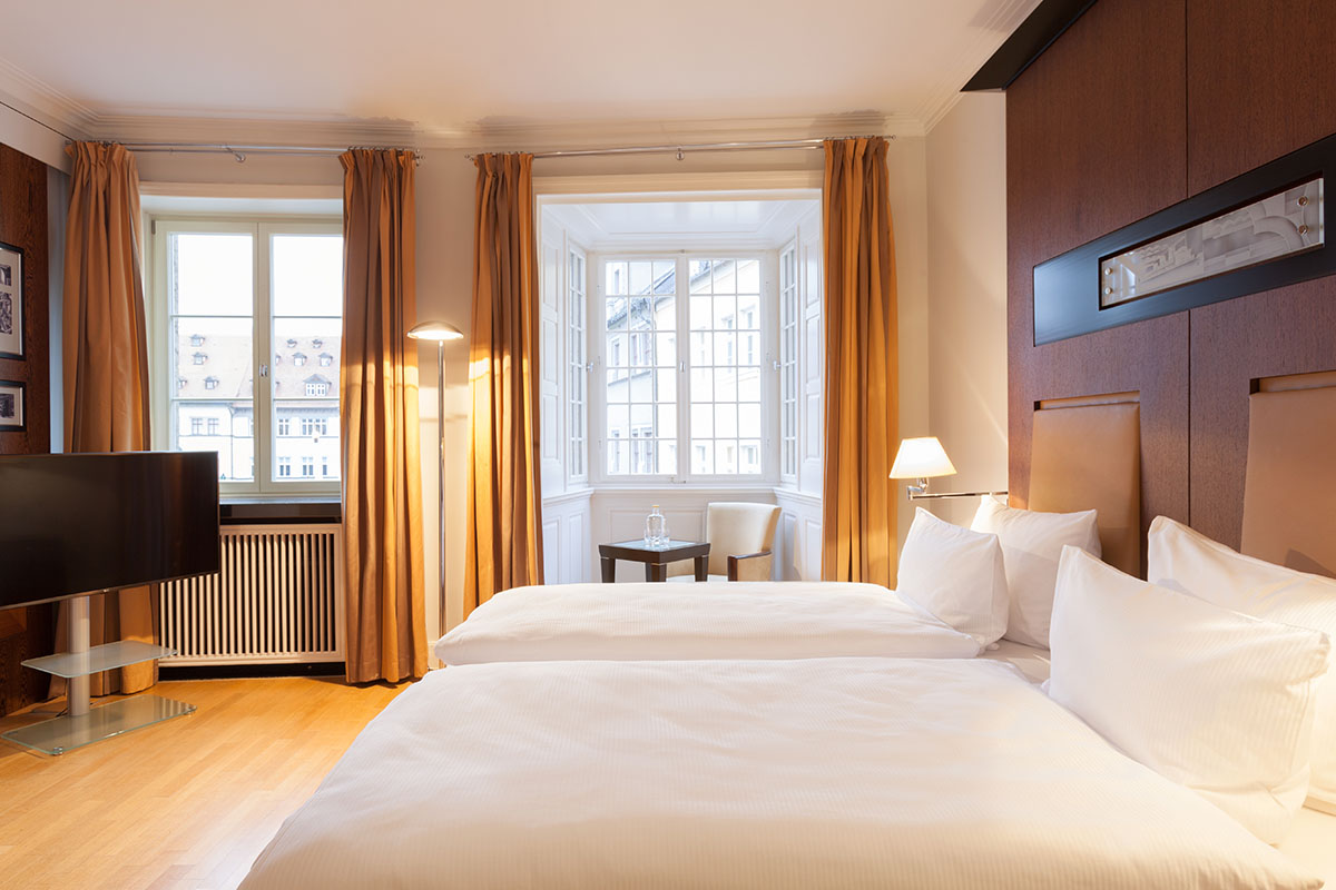 Bedroom of the Thomas Mann Suite in the Hotel Elephant Weimar with two luxurious beds, warm light and elegant design.