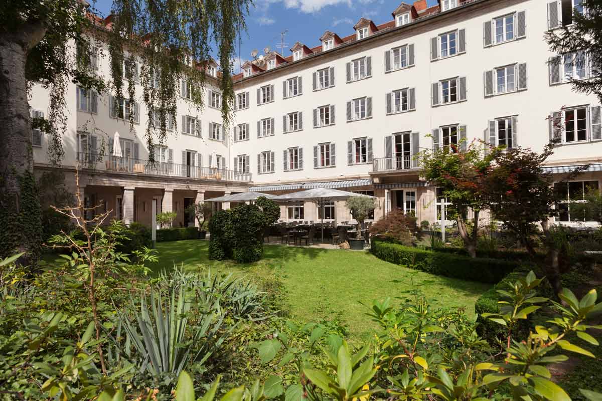 Der Garten des Hotel Elephant Weimar mit sattem Grün und dem imposanten Hotelgebäude in klassischer Architektur.