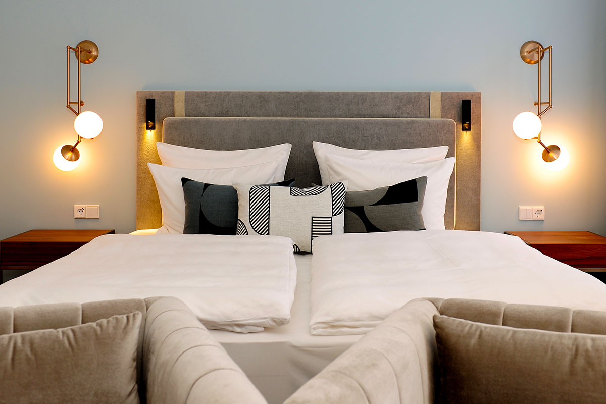 Modern double bed in the Grand Deluxe room of the Hotel Elephant Weimar with elegant lighting and soft pillows.