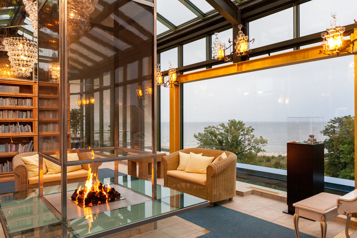 Winter garden at the Hotel Kaiserhof Heringsdorf with cozy armchairs, open fire, bookshelves and panoramic views of the Baltic Sea.