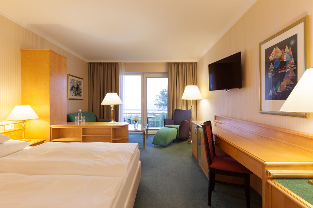 Hotel room at the Hotel Kaiserhof Heringsdorf with double bed, desk, seating area, TV and access to the balcony with sea view.