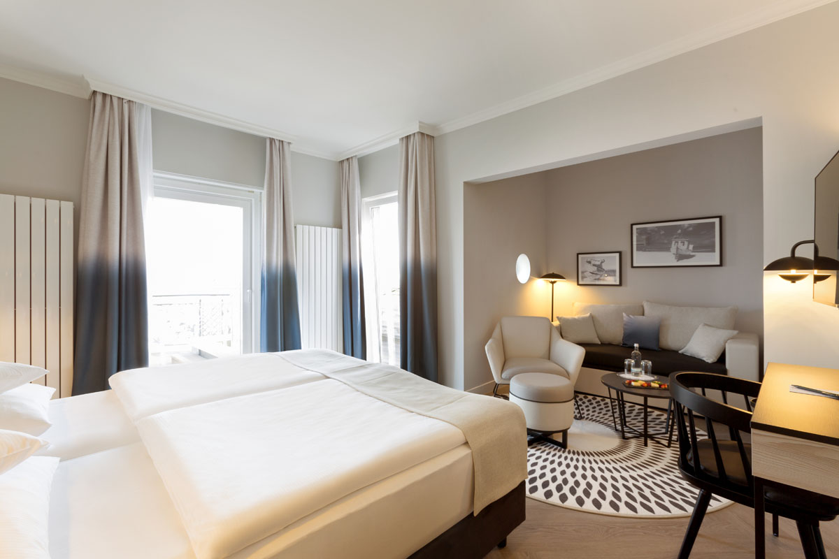 Blick in eine Themensuite mit Schlafbereich, Sofa, Sessel und Esstisch im Hotel Kaiserhof Heringsdorf auf Usedom.