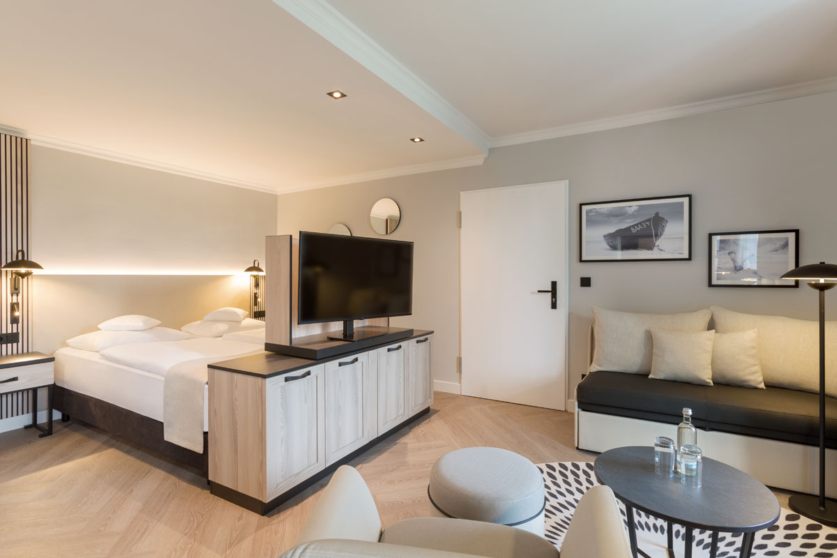 Überblick über die Themensuite mit Doppelbett, Fernseher und Sitzbereich in modernem Design im Hotel Kaiserhof Heringsdorf.