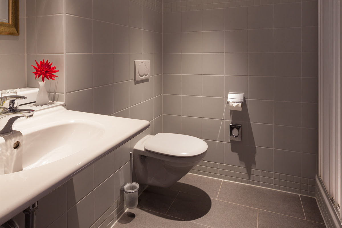 Modernes Badezimmer im Classic-Doppelzimmer mit Waschbecken, WC und grauen Fliesen im Hotel Kaiserhof Heringsdorf.