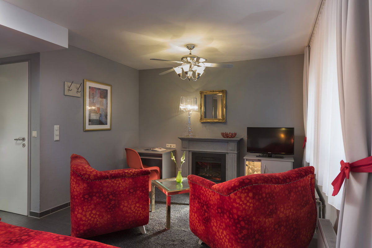 Sitzbereich im Familienzimmer mit zwei roten Sesseln, Kamin und Spiegel für Gemütlichkeit im Familienurlaub im Hotel Kaiserhof.