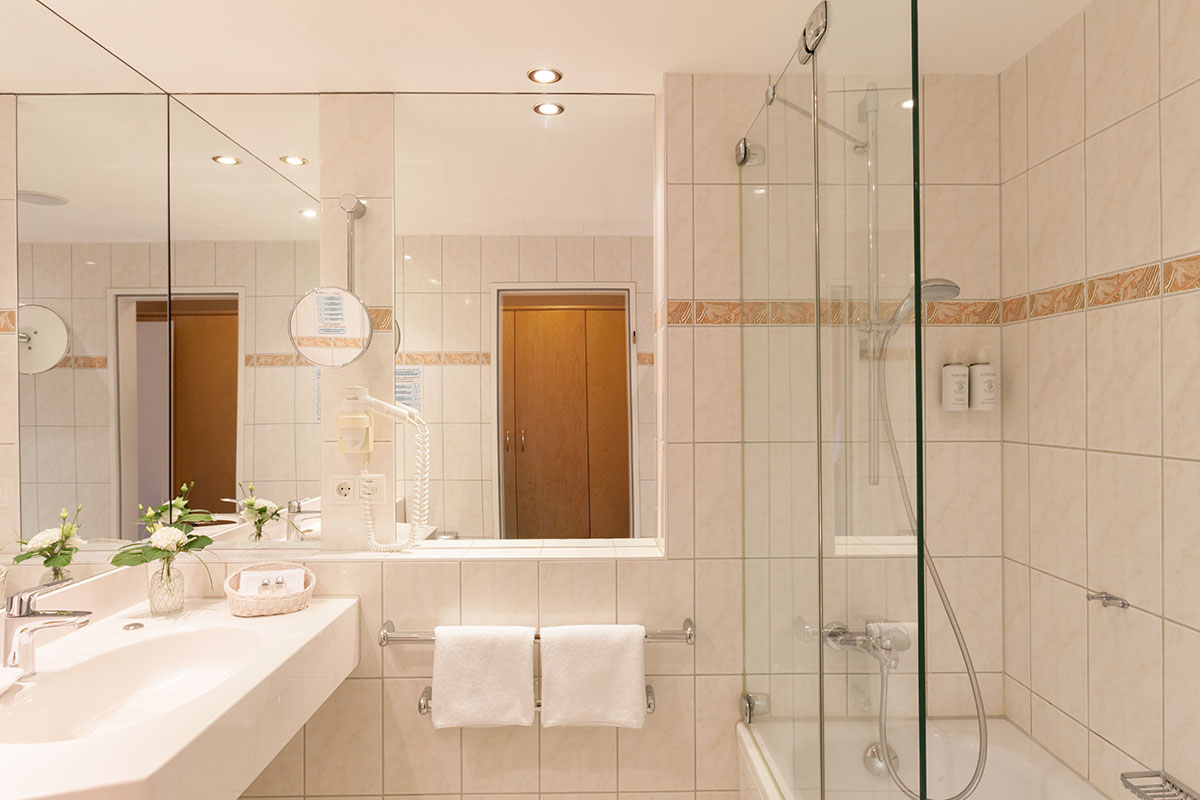 Großzügiges Badezimmer mit Badewanne, Spiegelwand und weißen Fliesen im Doppelzimmer mit Balkon im Hotel Kaiserhof.