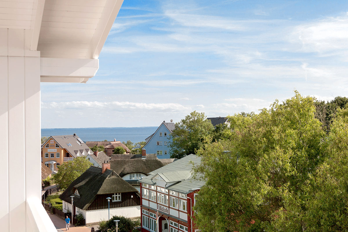 Blick vom Koopmanns Hotel über bunte Häuser und Reetdächer auf die Ostsee im Rahmen des Sommer Specials