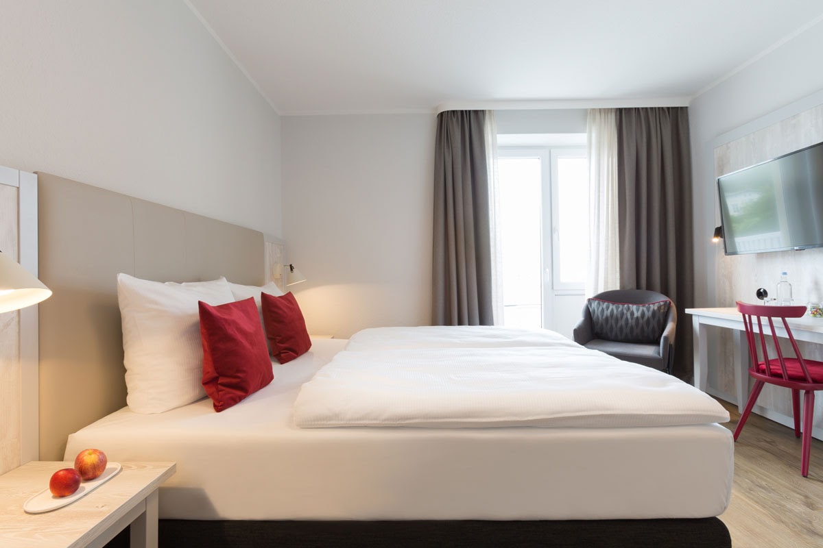 Bright double room at the Koopmanns Hotel with modern interior, equipped with bed, armchair, desk and large window.