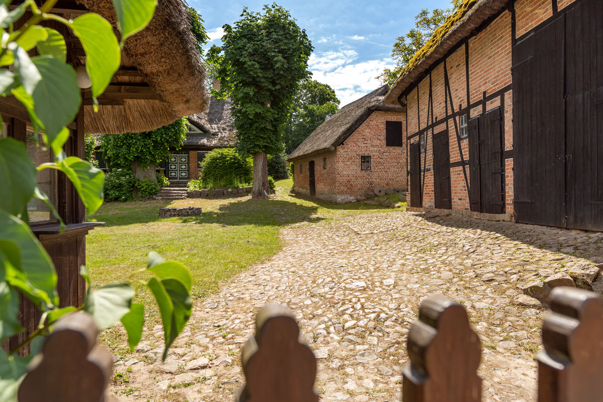 Historic half-timbered houses with thatched roofs, nestled in a green landscape and sunny inner courtyard with cobblestones.