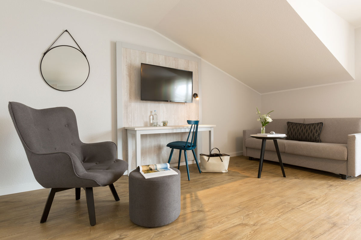 Seating area of a hotel room in the Koopmanns Hotel with gray sofa, armchair, table, desk and decorative mirror.