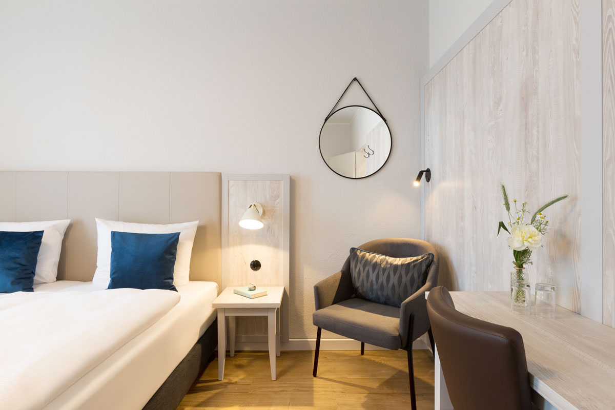 Inviting double room at the Koopmanns Hotel with stylish furnishings, armchair and decorative mirror on the wall.