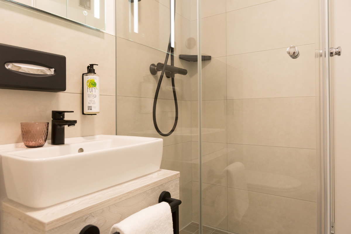 Modernes Badezimmer mit ebenerdiger Dusche, Waschbecken und Spiegel im Koopmanns Hotel &amp; Lädchen.