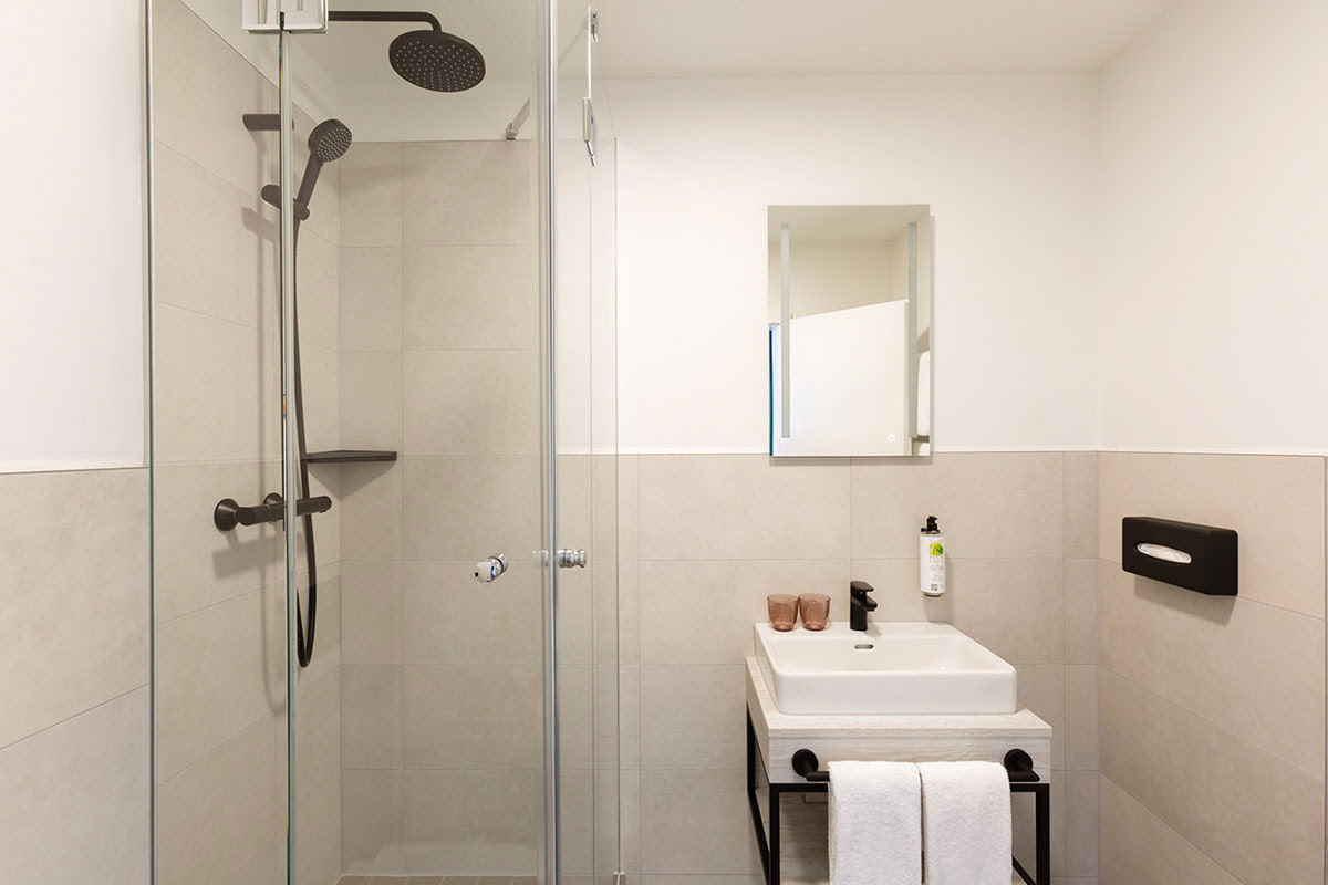 Badezimmer mit Regendusche, Waschbecken und modernem Design für Entspannung im Koopmanns Hotel.