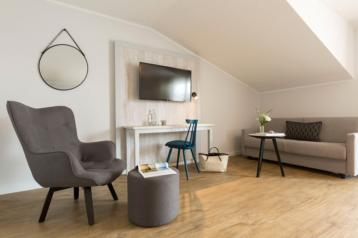 Gemütlicher Wohnbereich des Superior-Doppelzimmers im Koopmanns Hotel mit Sessel, Sofa, Schreibtisch und Fernseher.