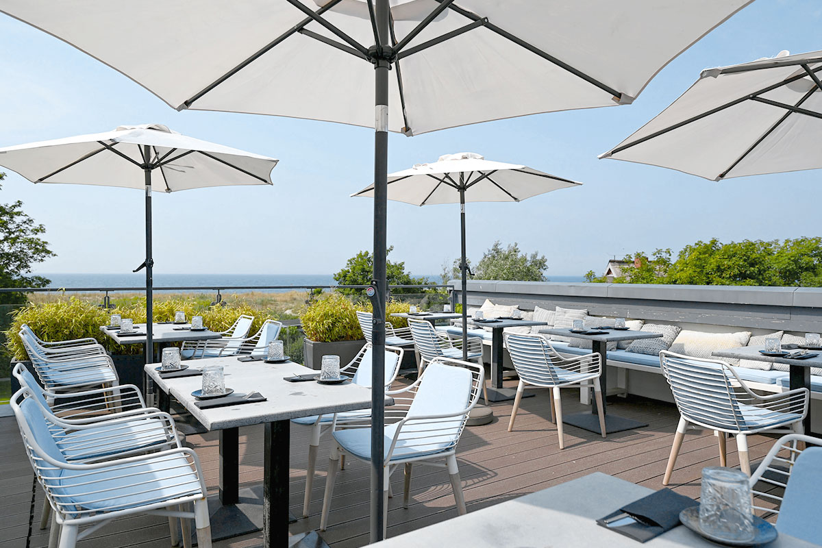 Elegant restaurant terrace at Künstlerquartier Seezeichen Ahrenshoop with white sun umbrellas and view of the Baltic Sea