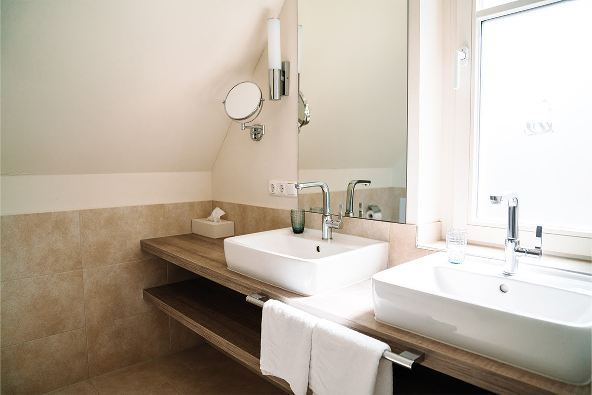 Bright bathroom in the Dünenpark vacation apartment in Hotel Künstlerquartier Seezeichen with double washbasin and natural light.