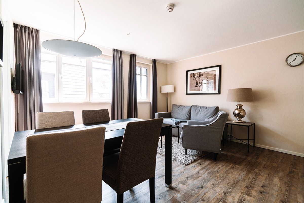 Wohnbereich mit Esstisch, gemütlichem Sofa und hellen Fenstern in der Ferienwohnung Strandblick im Dünenpark Ahrenshoop.