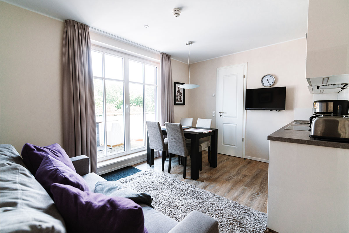 Modern living area with couch, dining table and natural light in the Stranddüne vacation apartment in the Hotel Künstlerquartier Seezeichen.