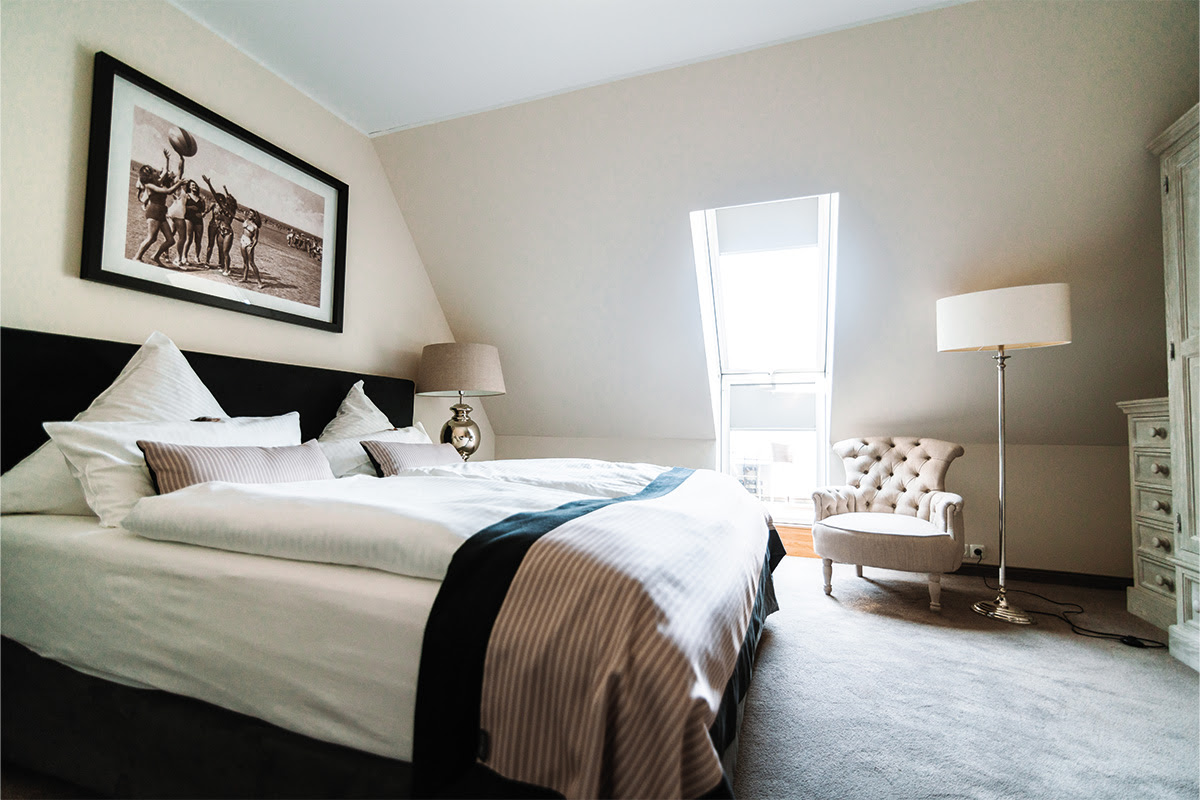 Bedroom with double bed, armchair and sloping roof in the Strandperle vacation apartment in the Hotel Künstlerquartier Seezeichen.