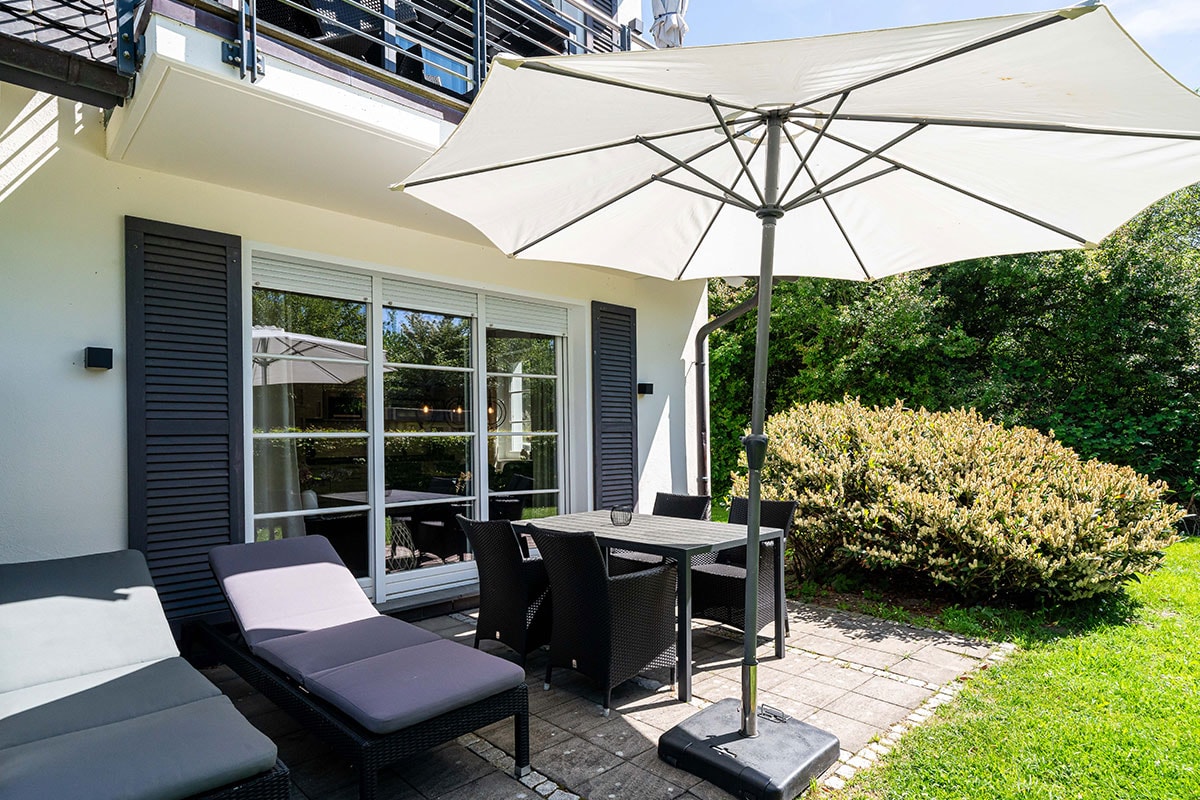 Terrasse mit Esstisch, Stühlen, Sonnenschirm und zwei Liegen vor der Ferienwohnung Seeschwalbe im Künstlerquartier Seezeichen.