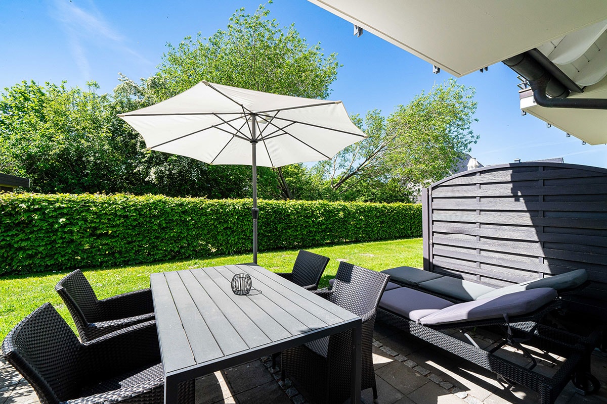 Private Terrasse der Ferienwohnung Seeschwalbe im Hotel Künstlerquartier Seezeichen mit Tisch, Sonnenliegen und Schirm.
