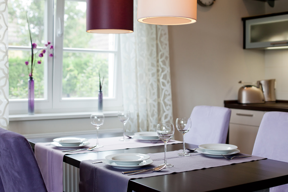 Stylishly laid dining table with four chairs and purple decorations in the Strandmöwe vacation apartment in the Hotel Künstlerquartier Seezeichen.