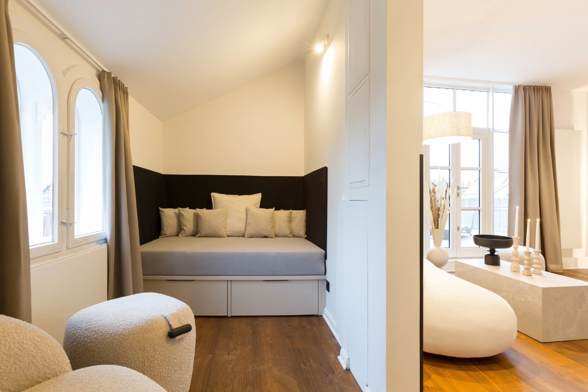 Helles Tagesbett mit Kissen, flankiert von großen Fenstern und Vorhängen in der Elisabeth-Suite im Hotel Künstlerquartier Seezeichen.
