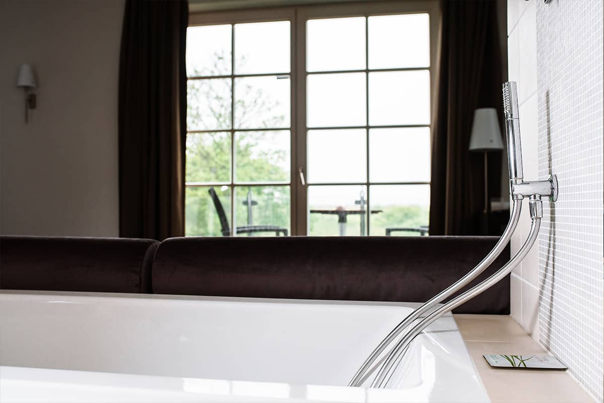 Free-standing bathtub in front of a large balcony door with a view of nature in the Deluxe Suite in the Hotel Künstlerquartier Seezeichen.