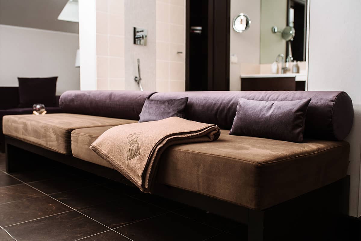Comfortable upholstered bench with decorative ceiling in the modern bathroom of the Deluxe Suite in the Hotel Künstlerquartier Seezeichen.
