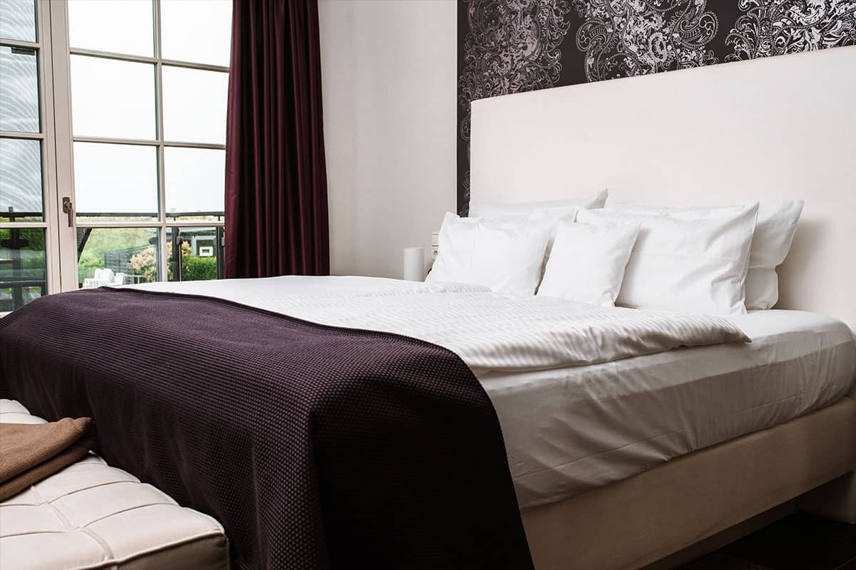 Large bed with white pillows and dark purple bedspread in the Deluxe Suite in the Hotel Künstlerquartier Seezeichen.