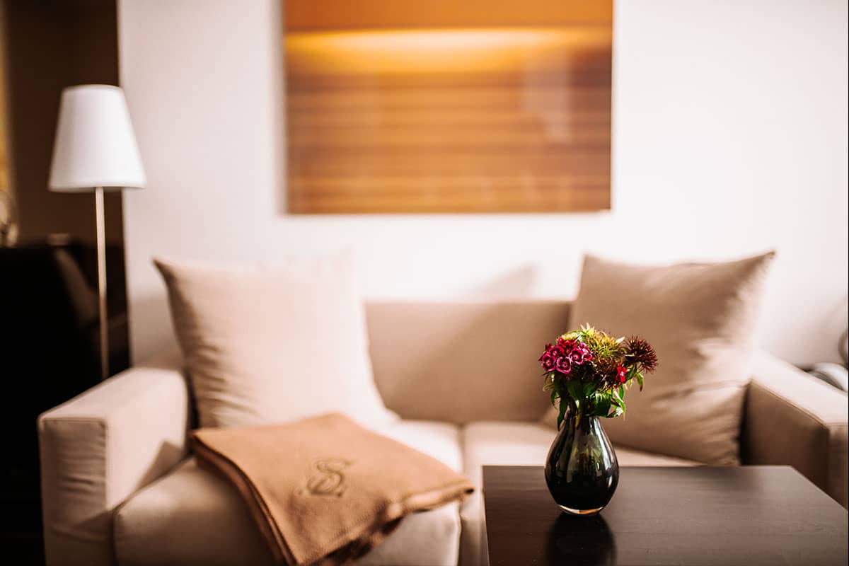 Gemütliche Couch in der Junior Suite im Hotel Künstlerquartier Seezeichen mit eleganter Decke und frischen Blumen auf dem Tisch.