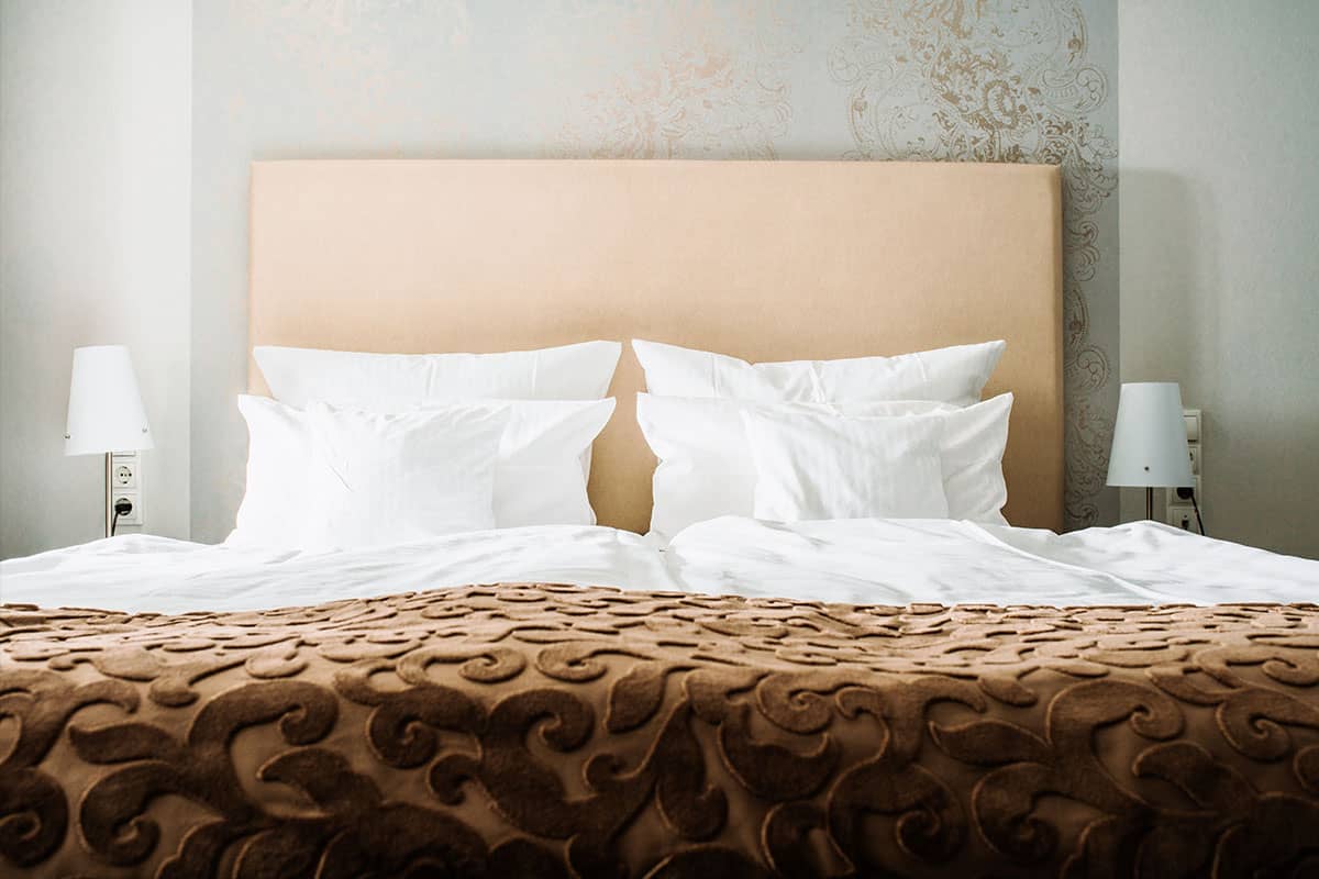 Kingsize-Bett mit weichen Kissen und einer eleganten braunen Decke der Junior Suite im Hotel Künstlerquartier Seezeichen.