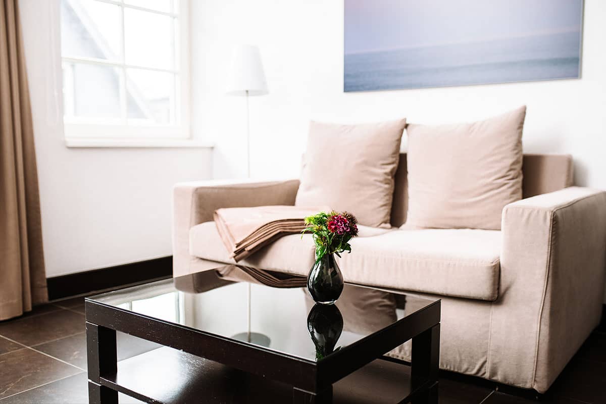 Sofa in der Junior Suite des Hotel Künstlerquartier Seezeichen mit hellem Design, Couchtisch und Blumenarrangement.