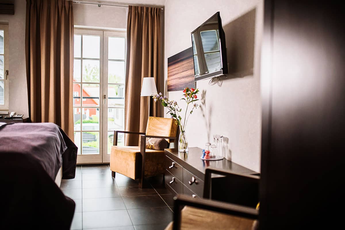 Gemütlicher Sitzbereich mit Sessel, Tisch und Blick durch die bodentiefen im Comfort Doppelzimmer des Künstlerquartier Seezeichen.