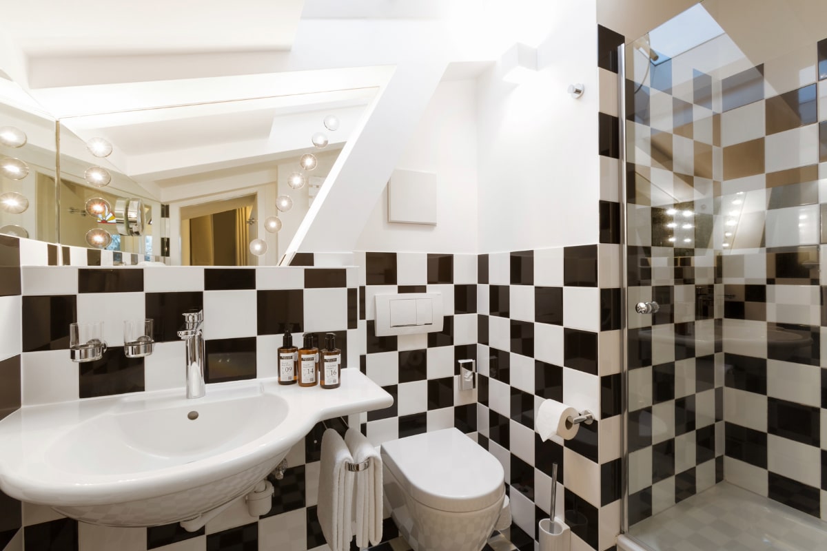 Modernes Badezimmer mit Schachbrettmusterfliesen, Dusche, Waschbecken und stilvoller Beleuchtung im Elisabeth von Eicken Hotel.