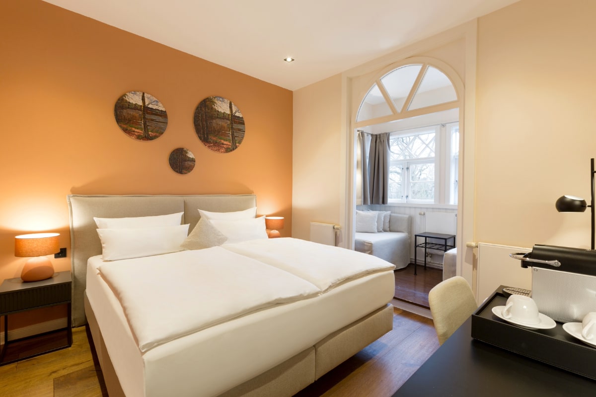 Doppelbett mit eleganten Nachttischen und warmen Farbakzenten im Doppelzimmer mit Meerblick im Elisabeth von Eicken Hotel.