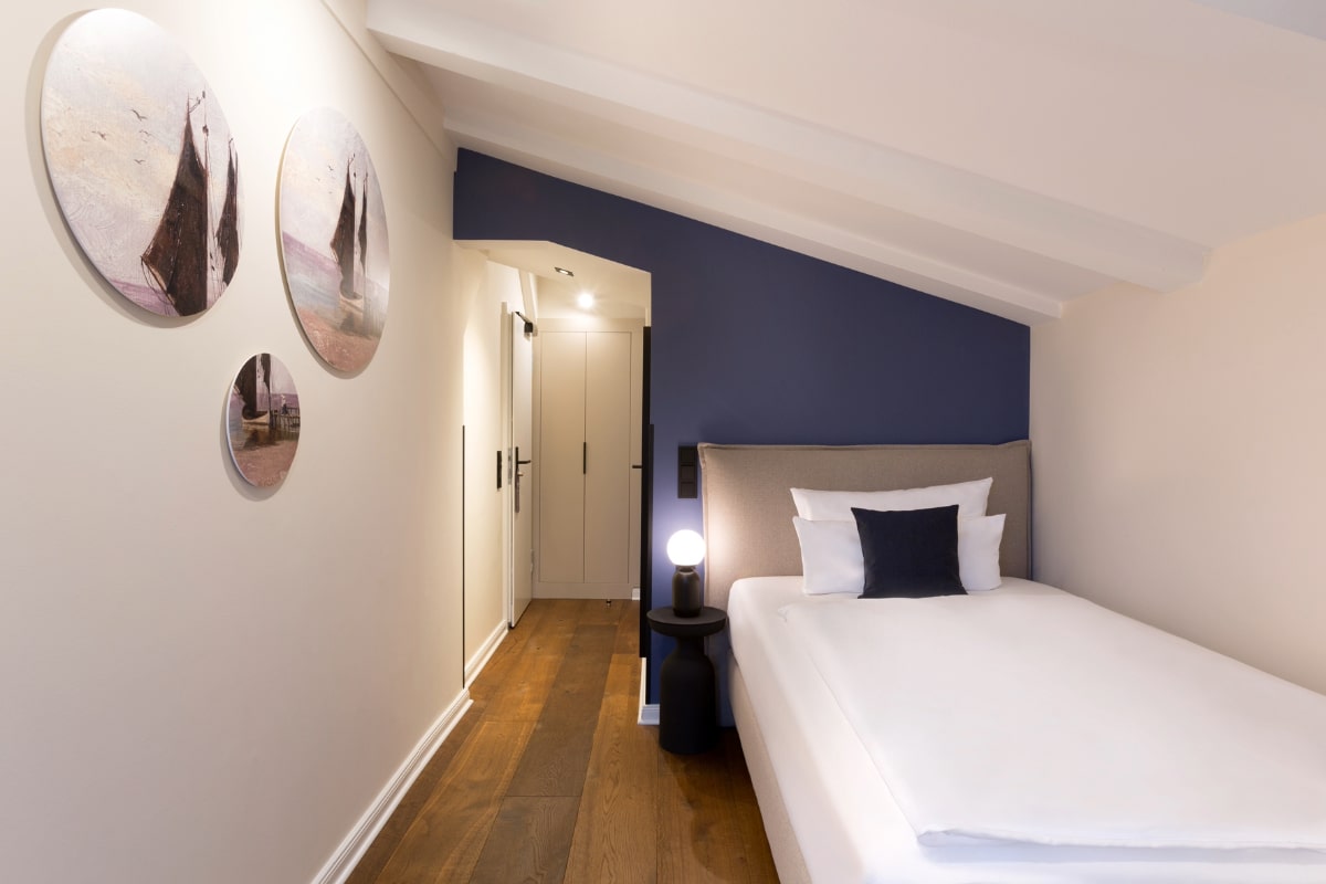Gemütliches Einzelzimmer mit Dachschrägen, maritimer Wanddekoration und modernem Bett im Elisabeth von Eicken Hotel.