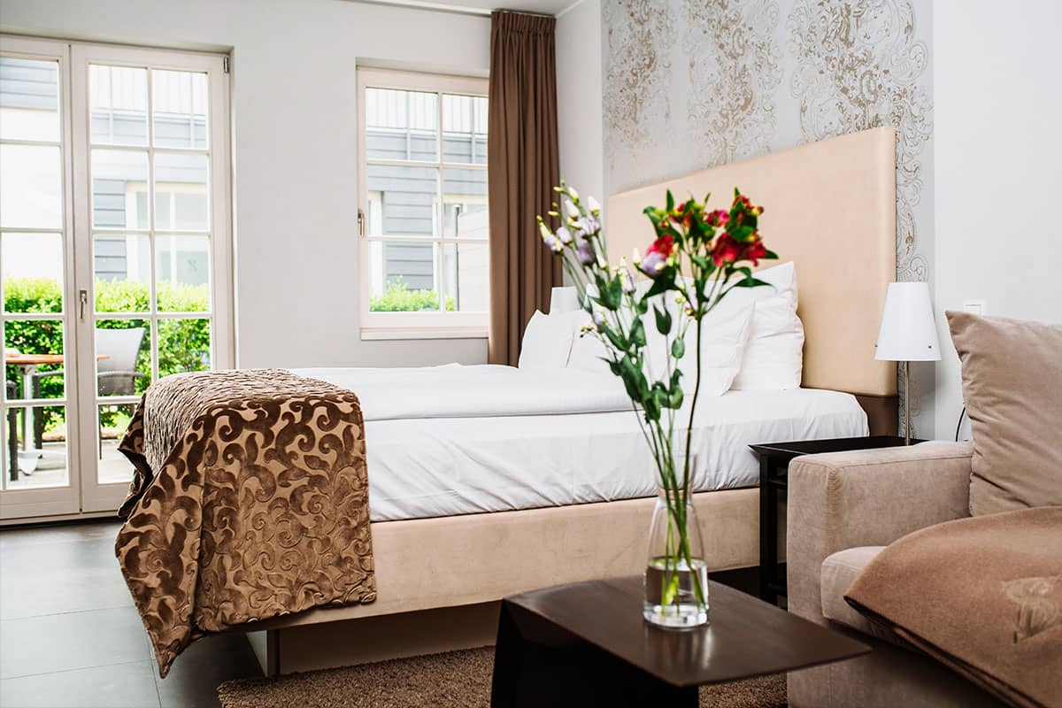 Komfortables Doppelbett im First-Class-Doppelzimmer im Hotel Künstlerquartier Seezeichen mit edler Einrichtung und Tageslicht.