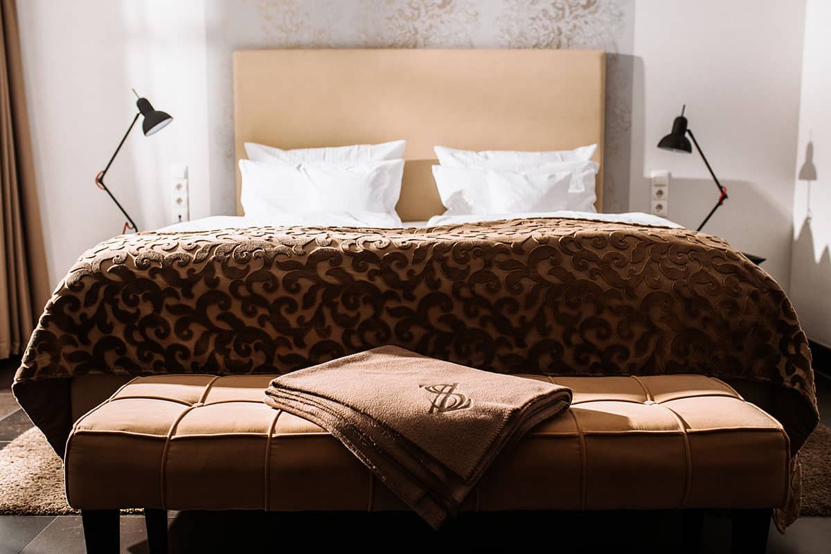 Doppelbett im First-Class-Doppelzimmer mit weicher Decke und stilvollem Kopfteil des Hotel Künstlerquartier Seezeichen.
