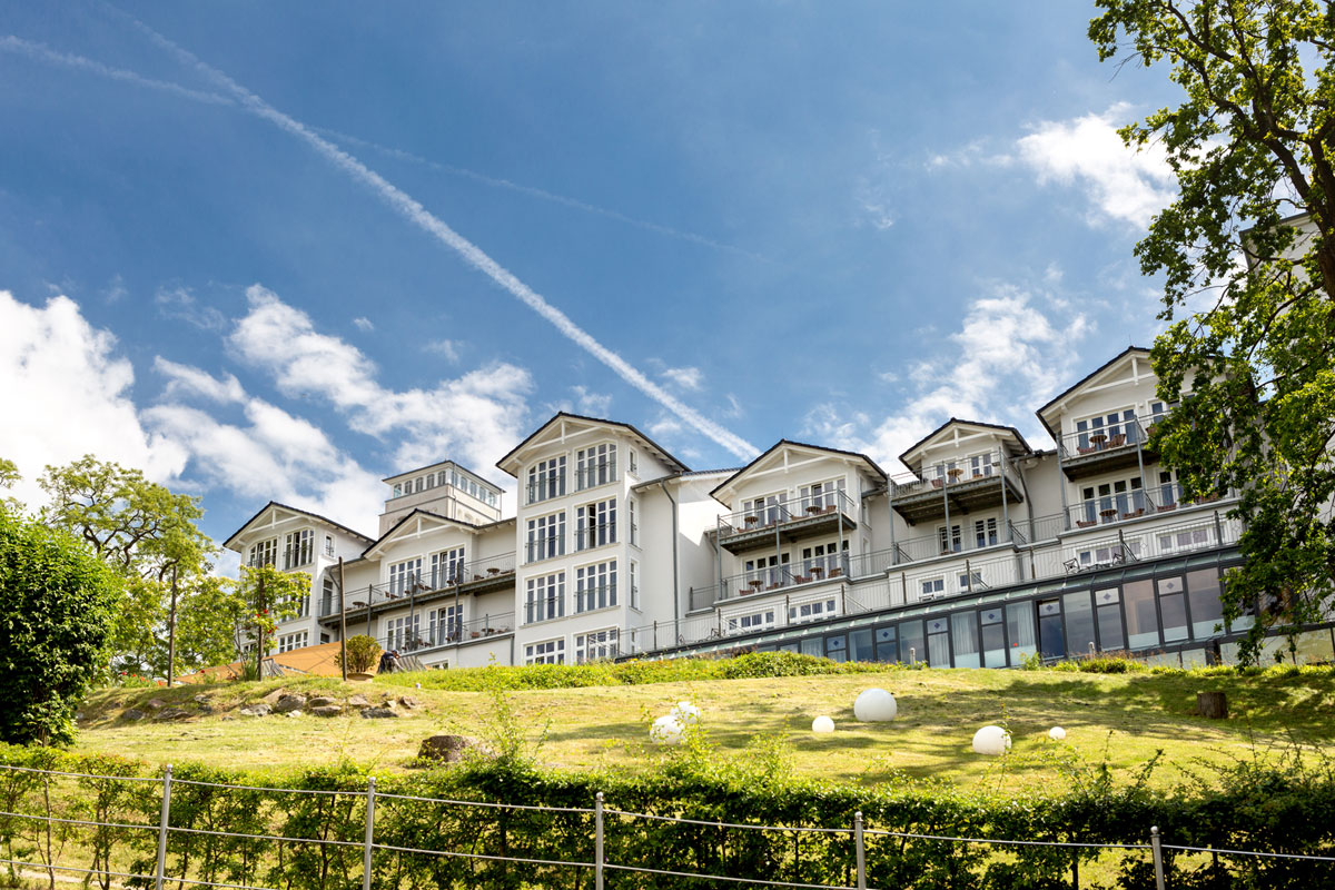 Exterior view of the Vju Hotel on Rügen, embedded in green nature, with impressive architecture and blue sky in the background.
