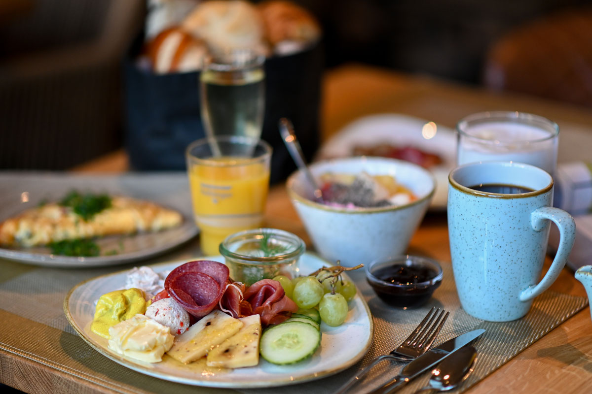 Breakfast at the Vju Hotel Rügen with fresh fruit, cheese, sausage, bread, omelette, yoghurt, coffee and orange juice on a laid table.